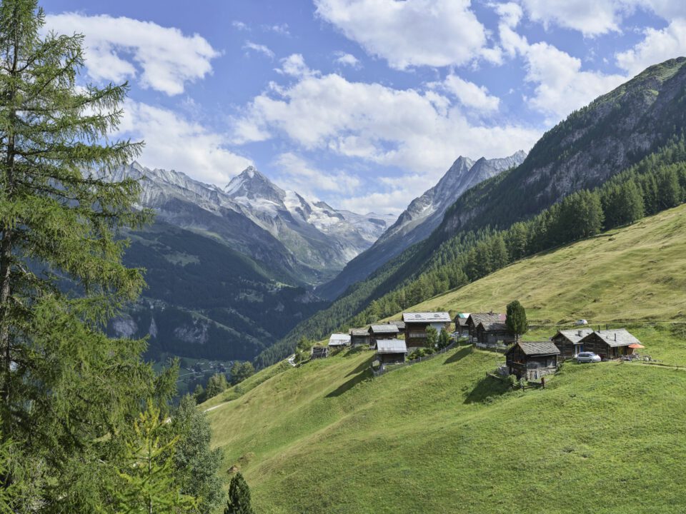 Chalets du hameau d’Arbey près d’Évolène, prairies et montagnes du Valais sous un ciel bleu.