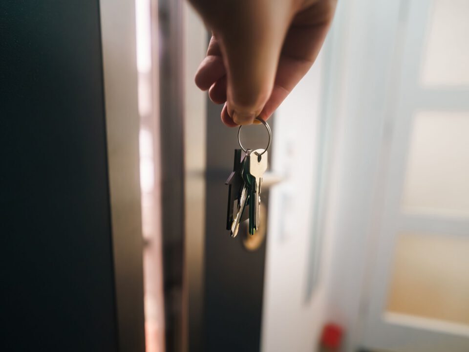Une main tenant les clés d’un logement devant une porte ouverte.
